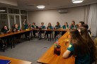 Młodzież siedząca przy stołach ustawionych na przeciw siebie. Prawie wszyscy mają takie same koszulki. Na stołach przekąski i picie. Jedna z dziewczyn unosi prawą rękę w górę.