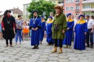 Na zdjęciu osoby ubrane w długie niebiesko-żółte suknie oraz inne stroje . Na drugim planie uczestnicy wydarzenia, miejska zabudowa i drzewo.  