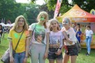 Na zdjęciu cztery młode dziewczyny pozujące do zdjęcia. Ich twarze i ubrania są ubrudzone kolorowymi proszkami. W tle widać innych uczestników wydarzenia, namioty i drzewa.  