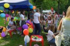 Na zdjęciu dzieci i dorośli przy i pod namiotem z kolorowymi balonami. W tle widać drzewa. 