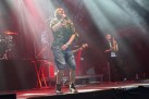 Na scenie muzycy podczas swojego występu. Całość oświetlona jest czerwonym światłem. 