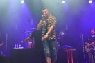 Na zdjęciu widać wokalistę i instrumentalistów. Całość oświetla niebieskie światło. 