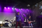 Na scenie trzej muzycy. Każdy z nich ma ubrane ciemne okulary. Jeden muzyk śpiewa, kolejny gra na gitarze elektrycznej, zaś trzeci muzyk gra na keyboardzie. Widać również inne instrumenty muzyczne jak gitara akustyczna, czy perkusja. Scenę oświetla fioletowe światło. 
