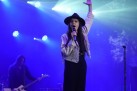 Na pierwszym planie kobieta śpiewająca do mikrofonu, zaś w tle gitarzysta. Całość oświetla niebieskie światło. 