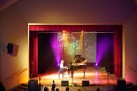 Na scenie Strzeleckiego Ośrodka Kultury młoda pianistka wykonuje utwór na fortepianie, a tło z kolorowym oświetleniem i projekcją lasu tworzy nastrojową, artystyczną atmosferę.