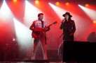 Na scenie gitarzysta i wokalistka podczas swojego występu. Scenę oświetla czerwone światło. 