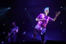 Na zdjęciu wokalistka i muzyk grający na gitarze. Kobieta w  jednej ręce trzyma mikrofon, drugą zaś wyciąga przed siebie. Cała scena jest oświetlona niebieskimi światłami. 