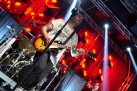 Na zdjęciu gitarzysta, za nim perkusja. Tło stanowi czerwone światło. 
