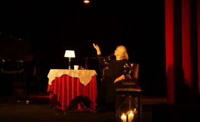 Na scenie Stanisława Celińska podczas jubileuszowego koncertu siedzącą na stylowym fotelu, obok niej stoi stół nakryty czerwonym obrusem, na którym leży biała koronkowa ceratka, na stole stoi również niewielka lampka, w tle znajduje się ozdobna, duża lampa o klasycznym designie