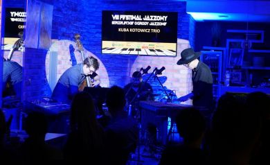 Kuba Kotowicz Trio podczas koncertu na niebieskim tle.