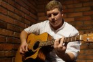 Mężczyzna w białej wzorzystej koszuli gra na gitarze. 