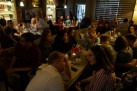 Na zdjęciu osoby biorące udział w wernisażu wystawy siedzą przy stolikach w restauracji i rozmawiają. 