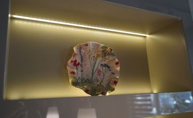 Na zdjęciu element ceramiczny w oświetlonej wnęce. Naczynie jest zdobione w wzory roślinne i kwiatowe.  - powiększ