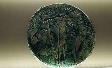 Na zdjęciu owalny, zielony element ceramiczny, o nieregularnych kształtach z wzorami roślinnymi.  - powiększ