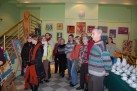 Na zdjęciu uczestnicy wydarzenia. Wokół nich obrazy oraz stół z zastawą do kawy i herbaty. 