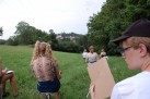 Zdjęcie przedstawia grupę młodych ludzi siedzących na krzesłach wśród zieleni, rysują.