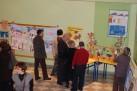 Na zdjęciu osoby biorące udział w wernisażu. Jedna z kobiet robi zdjęcie aparatem. 