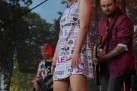 Kobieta w wzorzystej sukience i wysokich butach, a także dwóch mężczyzn grających na gitarach podczas występu na scenie.