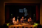 Na zdjęciu widać koncert zespołu Renata Przemyk TRIO, odbywający się na scenie w sali widowiskowej. Muzycy grają na gitarach i innych instrumentach i śpiewają przy nastrojowym oświetleniu.