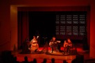 Na zdjęciu widać koncert zespołu Renata Przemyk TRIO, odbywający się na scenie w sali widowiskowej. Muzycy grają na gitarach i śpiewają przy nastrojowym oświetleniu. Widać część publiczności.