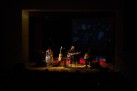 Na zdjęciu widać koncert zespołu Renata Przemyk TRIO, odbywający się na scenie w sali widowiskowej. Muzycy grają na gitarach i śpiewają przy nastrojowym, przyciemnionym oświetleniu, a przed nimi siedzi publiczność pogrążona w ciemności.