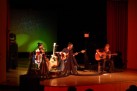 Na zdjęciu widać koncert zespołu Renata Przemyk TRIO, odbywający się na scenie w sali widowiskowej. Muzycy grają na gitarach i śpiewają przy nastrojowym oświetleniu. 