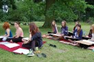 Na zdjęciu widać grupę młodych ludzi, siedzących na trawie i rysujących. W tle widać owce pasące się na łące. Na pierwszym planie znajduje się kilka osób, które siedzą na kocach lub matach i szkicują. Mają przy sobie bloki rysunkowe i ołówki. Scena rozgrywa się na zewnątrz, w zielonym, trawiastym terenie, otoczonym drzewami. W tle, po lewej stronie, widać kilka owiec.