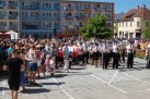 Tłum ludzi zgromadzony na placu miejskim. Wśród ludzi widać grającą orkiestrę dętą.  