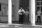 Czarno-białe zdjęcie mężczyzny przemawiającego do mikrofonu, stoi na schodach ratusza. Na drugim planie dwaj inni mężczyźni . 