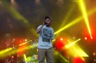 Występ wokalisty na scenie. W tle kolorowe światła emitowane przez reflektory. 