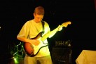 Mężczyzna grający na gitarze elektrycznej. Oświetla go żółte światło. 