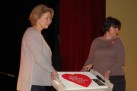 Dwie kobiety trzymające tort przyozdobiony dużym, czerwonym sercem z napisem ,,Wielka Orkiestra Świątecznej Pomocy'. 