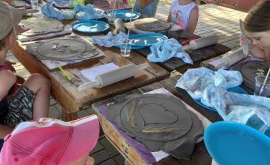 Na zdjęciu dzieci siedzące przy stole podczas warsztatów ceramicznych.  - powiększ
