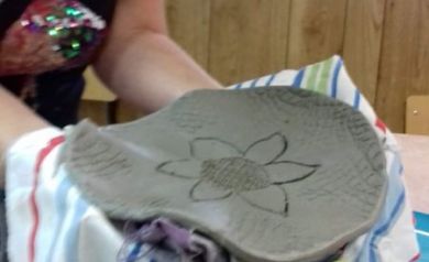 Na zdjęciu widać osobę trzymającą na tkaninie w kolorowe paski element ceramiczny z wzorem kwiatu.  - powiększ