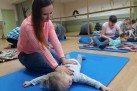Dzieci leżące na matach lub kocach. Dorośli wykonują masaż pleców dzieciom. W tle lustra na ścianie.