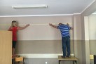Kobieta i mężczyzna w stoją na stołach i naklejają taśmę na ścianie. 