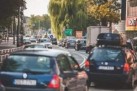 Zdjęcie przedstawia ulicę pełną samochodów. Z boku widać również zabudowę miasta w postaci sklepów. Na zdjęciu widnieje fragment miasta Strzelce Opolskie. 