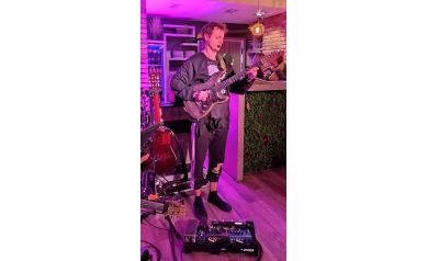 Mężczyzna grający na gitarze na tle fioletowych barw.