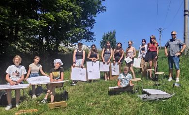 Grupa młodych artystów i ich instruktor spontanicznie pozuje do pamiątkowego zdjęcia. To wspólna pamiątka z dni spędzonych na malarskim plenerze, gdzie pasja do sztuki łączy ludzi.