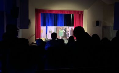 Na pierwszym planie widownia, natomiast na drugim dwóch aktorów na scenie podczas teatrzyka dla dzieci 'Świąteczny Cud'