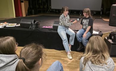 Na zdjęciu kobieta przeprowadzająca wywiad z uczestniczką projektu. Na pierwszym planie widać również resztę osób biorących udział w spotkaniu - są odwrócone tyłem do aparatu. - powiększ