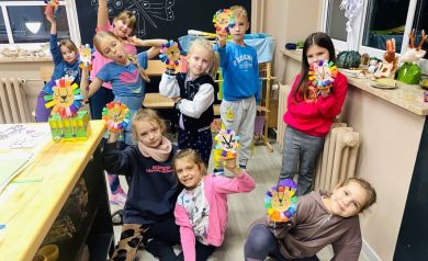 Zdjęcie grupowe dzieci biorących udział w kreatywnych zajęciach. W dłoniach trzymają wykonane przez siebie kolorowe lwy. 