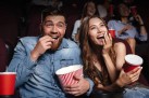 Na zdjęciu widać ludzi w kinie, którzy jedzą popcorn i śmieją się podczas seansu.