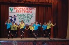 Na zdjęciu widać grupę młodych tancerzy występujących na scenie podczas V Powiatowego Festiwalu 'Tańczyć Każdy Może', który odbył się w 2008 roku. W tle widoczny jest baner z nazwą festiwalu. Grupa składa się z kilku osób ubranych w turkusowe i żółte koszulki oraz czarne spodnie.