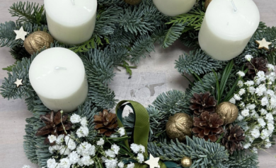 Na zdjęciu wieniec adwentowy z białymi świecami i biłą gipsówką, można dostrzec również inne dekoracyjne elementy takie jak złote orzechy, szyszki, czy zielone kokardy. 