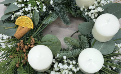 Wieniec adwentowy z białymi świecami i białą gipsówką. Znajdują się tam również inne dekoracje takie jak suszona pomarańcza, czy laski cynamonu. 