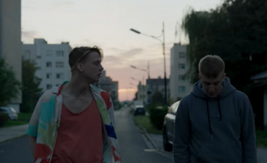 Scena z filmu. Dwóch młodych mężczyzn spaceruje po ulicach osiedla. Prowadzą dialog.