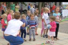 Na zdjęciu widać grupę małych dzieci bawiących się na placu podczas plenerowego wydarzenia, pod opieką dorosłych. Dzieci trzymają kolorowe balony i piłki.