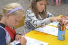 Na zdjęciu dwie dziewczynki siedzące przy żółtych stolikach malują kredkami po kolorowankach. 