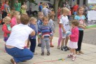 Na zdjęciu widać grupę małych dzieci bawiących się na placu podczas plenerowego wydarzenia, pod opieką dorosłych. Dzieci trzymają kolorowe balony i piłki.